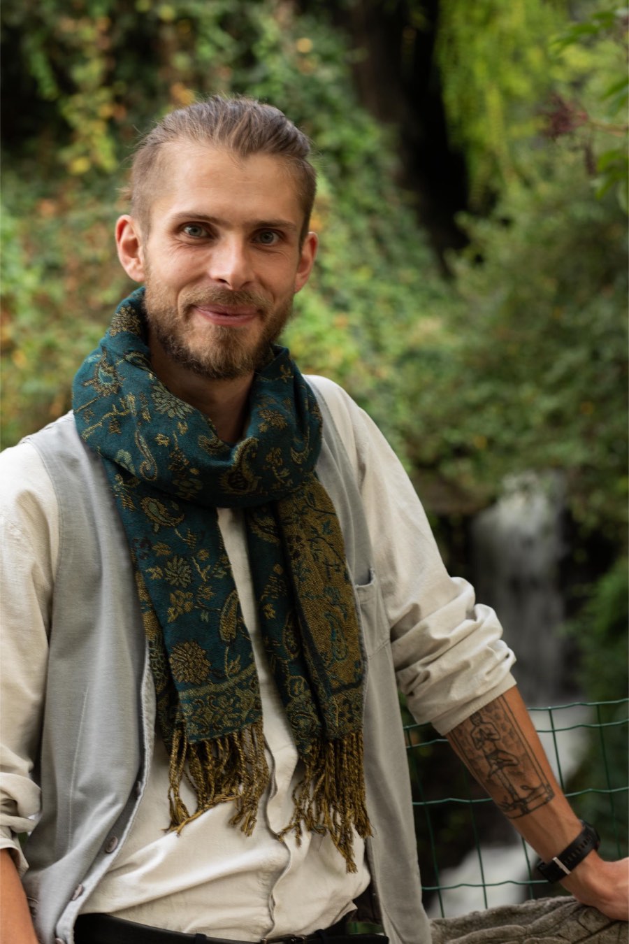 Ben Carey Donaldson, smiling, wearing a green scarf, in a forest